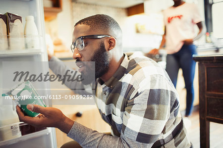 Young man reading label on container at refrigerator