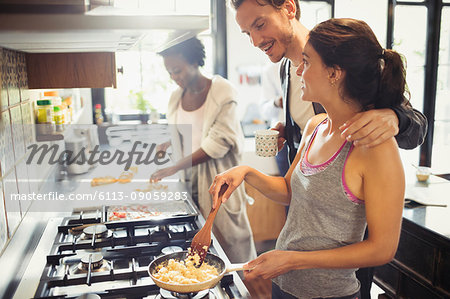 Young couple cooking scrambled eggs on stove in kitchen