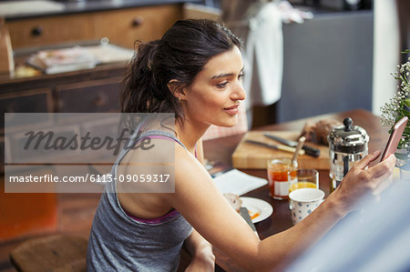 Young woman texting with smart phone at breakfast table