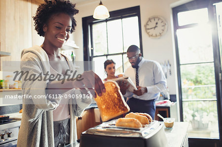 Smiling woman toasting bread in toaster in kitchen