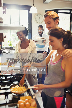 Friend roommates cooking scrambled eggs at stove in kitchen