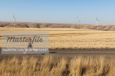 Man jogging on rural road, farmland and wind turbines in distance, Washington