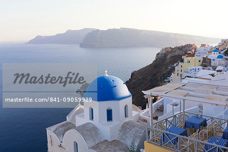 Evening view over the Caldera from Oia with blue domed church and distant volcanic cliffs, Santorini, Greek Islands, Greece, Europe