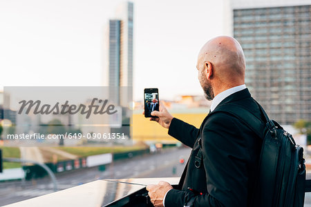 Mature businessman standing outdoors, taking selfie, using smartphone