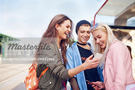 Three young female friends looking at smartphone at city tram station Three young female friends looking at smartphone at city tram station