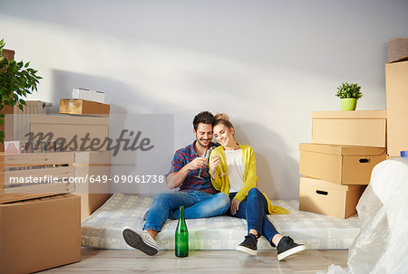 Young couple at home, surrounded by cardboard boxes, drinking champagne