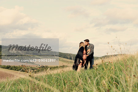 Romantic pregnant mid adult couple kissing on rural hillside
