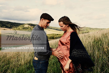 Romantic man with hands on pregnant wife's stomach on hillside