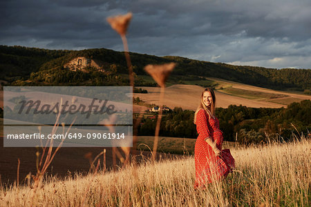 Portrait of happy pregnant woman in red dress on hillside