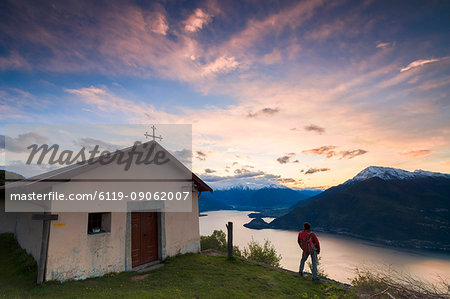 Hiker at the church of San Domenico admires Lake Como framed by pink sky at dawn, Cremia, Lombardy, Italian Lakes, Italy, Europe