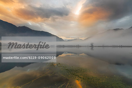 Mountains reflected in water at dawn shrouded by mist, Pozzo di Riva Novate, Mezzola, Chiavenna Valley, Lombardy, Italy, Europe