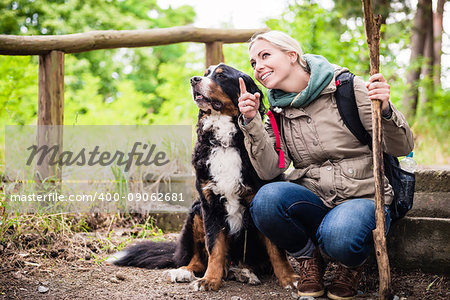 Hiking woman with rucksack and her bernese mountain dog on a trail