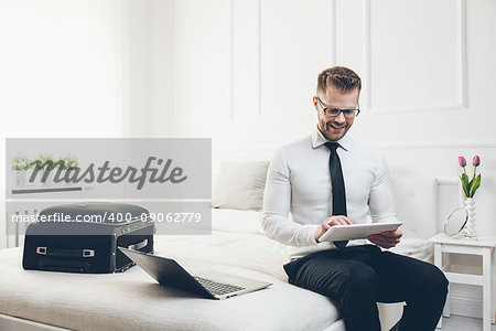 Young businessman on bed working with a tablet laptop from his hotel room