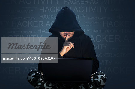 Man with hidden face working at a computer. Holding a finger to his mouth. Computer hacker stealing data from a laptop concept for network security, identity theft and computer crime