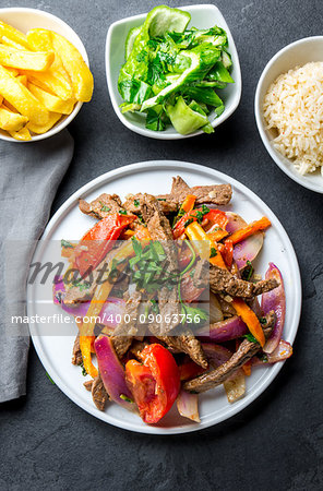 Peruvian dish Lomo saltado - beef tenderloin with purple onion, yellow chili, tomatoes served on white plate with french fries and rice. Top view