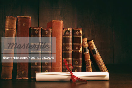 Stack of old books with diploma on wooden desk