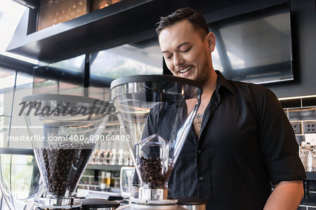 Happy young man preparing espresso from fresh roasted coffee beans while working as barista in a modern coffee shop