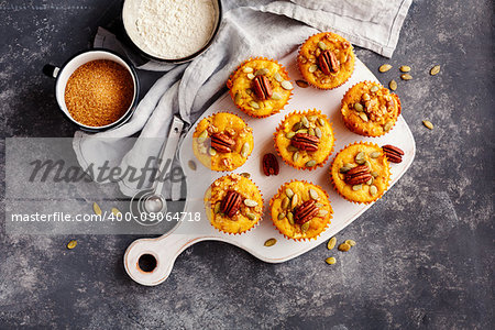 Freshly baked pumpkin muffins with pumpkin seeds and pecans on a cutting board.