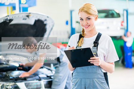 Male and female mechanic team examine car engine with light and checklist in workshop