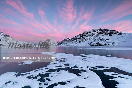 The frozen Lago Bianco framed by pink clouds at dawn, Bernina Pass, canton of Graubunden, Engadine, Switzerland, Europe