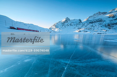 The Bernina Express train runs beside the frozen Lago Bianco, Bernina Pass, canton of Graubunden, Engadine, Switzerland, Europe