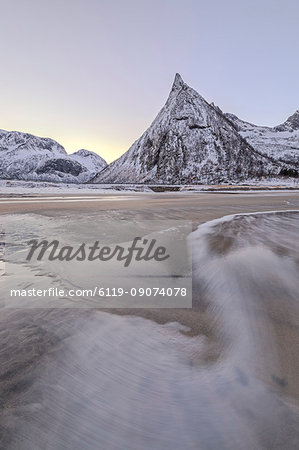 Snowy peaks and sandy beach framed by the icy waves of frozen sea at dawn, Ersfjord, Senja, Troms, Norway, Scandinavia, Europe