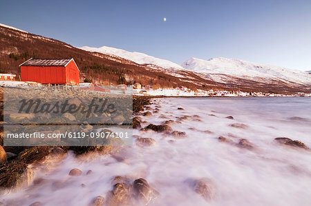 Waves of cold sea crashing on the rocks and typical wooden huts called Rorbu, Djupvik, Lyngen Alps, Troms, Norway, Scandinavia, Europe