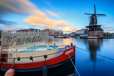 The fishing boat frames the Windmill De Adriaan reflected in the River Spaarne at dusk, Haarlem, North Holland, The Netherlands, Europe