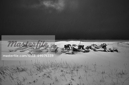 Fishing boats lying on dry land covered in snow and ice in winter.