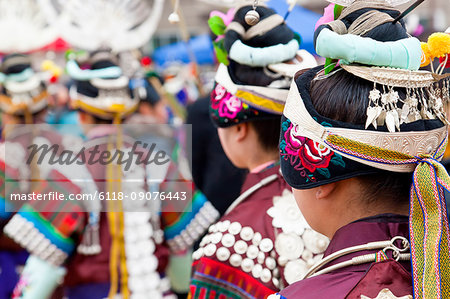 Rear view of girls wearing colourful traditional Chinese costumes and headdresses dancing at a festival.