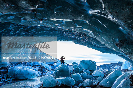 Rear view silhouette of person standing on ice rock at the entrance to a glacial ice cave.