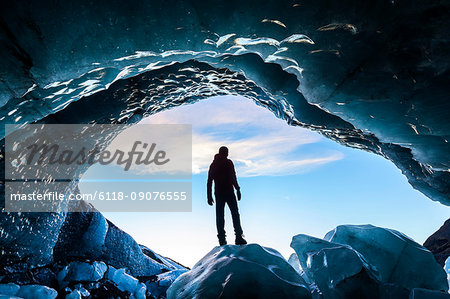 Rear view silhouette of person standing on ice rock at the entrance to a glacial ice cave.