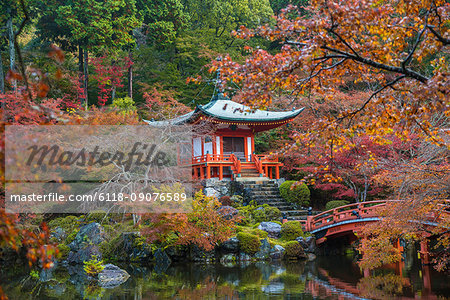 Park in autumn with traditional Japanese temple built on rocks, lake, bridge and trees.