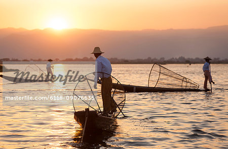 Traditional fisherman on a boat, holding fishing basket, fishing on lake at sunset.