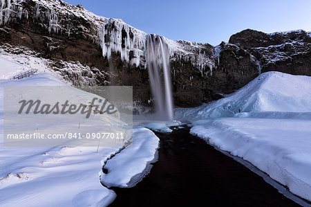 Winter view of Seljalandsfoss Waterfall at dusk with snow covered foreground and icicles hanging from cliffs, South Iceland, Polar Regions Winter view of Seljalandsfoss Waterfall at dusk with snow covered foreground and icicles hanging from cliffs, South Iceland, Polar Regions