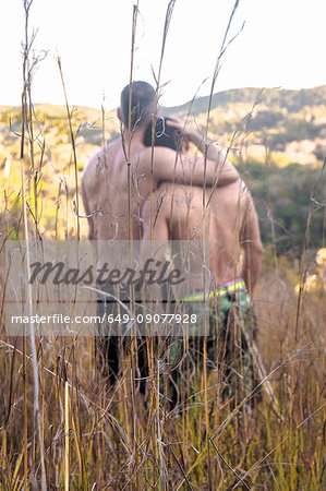 Rear view of two bare chested men looking out at landscape from long grass, Guaramiranga, Ceara, Brazil