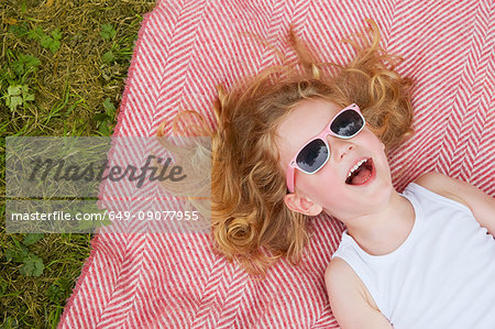 Overhead portrait of girl with blond hair and sunglasses posing on blanket