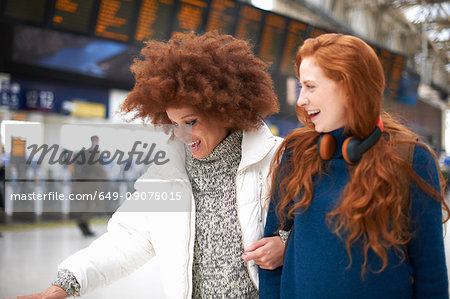 Two young women at train station, walking arm in arm