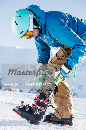 Mature man wearing skiwear, putting on ski boots