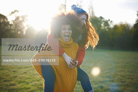 Two young women, in rural setting, young woman giving friend piggyback ride