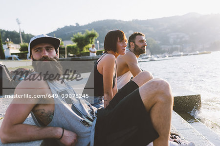 Three young hipsters sitting looking out at lake Como, Como, Lombardy, Italy