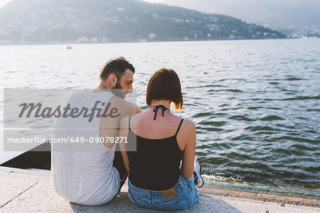 Rear view of young couple sitting on waterfront, Lake Como, Lombardy, Italy