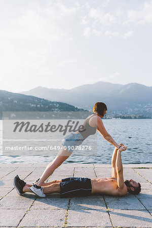 Young woman balancing with boyfriend lying on waterfront, Lake Como, Lombardy, Italy