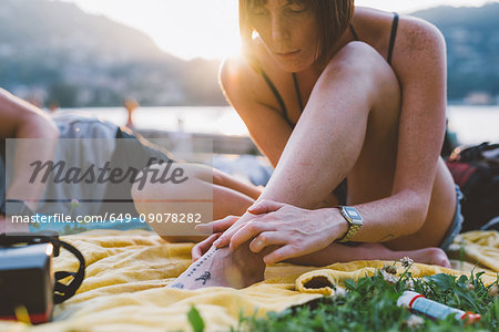 Young woman looking at foot tattoo on waterfront grass, Lake Como, Lombardy, Italy