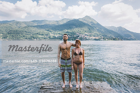 Portrait of couple in swimwear standing on water's edge Lake Como, Lombardy, Italy