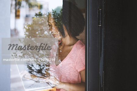 Woman in cafe window seat typing on laptop, Shanghai French Concession, Shanghai, China