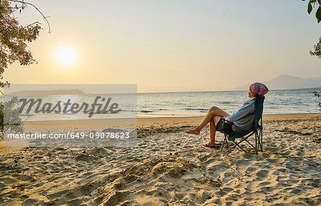 Woman on beach in deckchair looking away at sea, Florianopolis, Santa Catarina, Brazil, South America