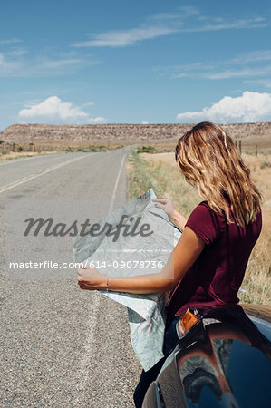 Woman leaning against car looking at map