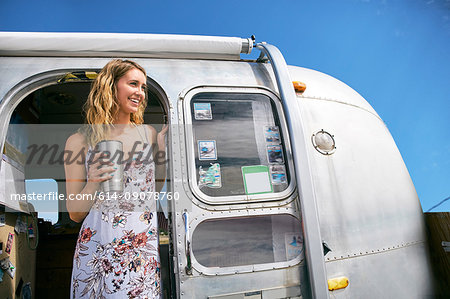 Young woman with coffee looking out from airstream doorway