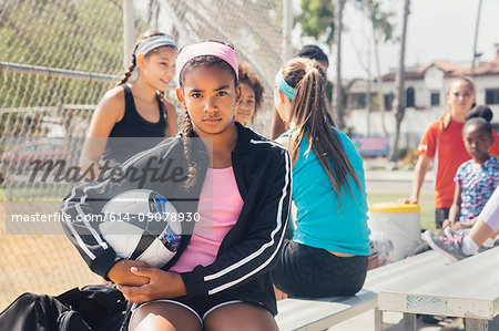 Portrait of schoolgirl amongst group holding soccer ball on school sports field